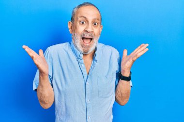 Sakallı yakışıklı, sıradan mavi gömlekli mutlu bir gülümsemeyle zaferi kutlayan ve elleri havada kazanan bir adam. 