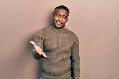 Balıkçı yaka kazak giyen genç siyahi bir adam dostça gülümseyerek selamlama ve hoş geldin diyor. başarılı iş. 