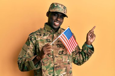 Genç Afro-Amerikan askeri üniforma giymiş elinde Amerikan bayrağı tutarak mutlu mesut gülümsüyor. 