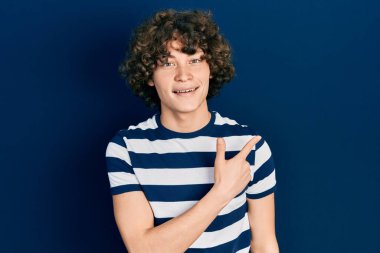 Yakışıklı, çizgili tişört giyen, neşeli yüzlü, elleri ve parmaklarıyla gülümseyen mutlu ve doğal bir ifade takınan genç bir adam. 