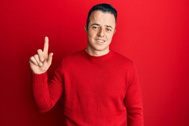 Kış süveteri giyen yakışıklı genç bir adam bir fikir ya da soruyla gülümsüyor ve mutlu bir yüzle işaret ediyor. 