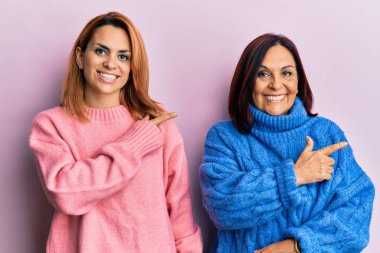 Latin anne ve kızı gündelik kıyafetler giyip gülümsüyor. Elleri ve parmakları yana doğru uzanıyor. 