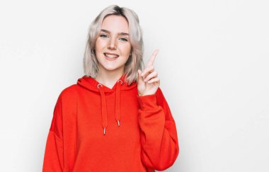 Gündelik kıyafetler giyen genç sarışın kız bir numarayı gösterip işaret ederken kendinden emin ve mutlu bir şekilde gülümsüyor.. 