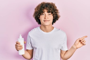 Kozmetik nemlendirici krem tutan yakışıklı genç adam gülümsüyor. 