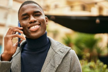 Genç Afrikalı Amerikalı gülümseyen mutlu bir adam şehirdeki akıllı telefondan konuşuyor.