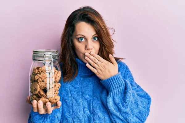 Jovem Caucasiana Segurando Frasco Biscoitos Chocolate Cobrindo Boca Com Mão — Fotografia de Stock