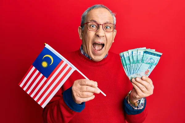 ハンサムなシニア男とともに白髪保持マレーシアフラグとマレーシアリンギット紙幣祝うクレイジーと驚きのために成功でオープン目叫んで興奮 — ストック写真