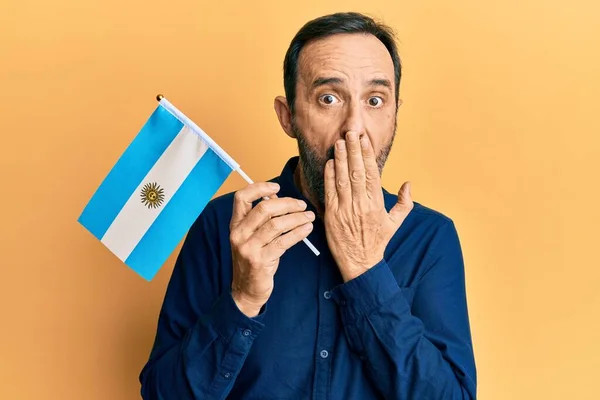 手で口を覆い 衝撃を与え 間違いを恐れて アルゼンチンの旗を持っている中世のパニックの男 驚きの表情 — ストック写真