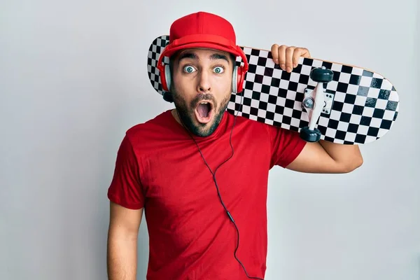 Young Hispanic Man Using Headphones Holding Skate Scared Amazed Open — Stock Photo, Image