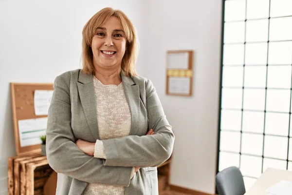 Middle age businesswoman smiling happy standing with arms crossed gesture at the office.