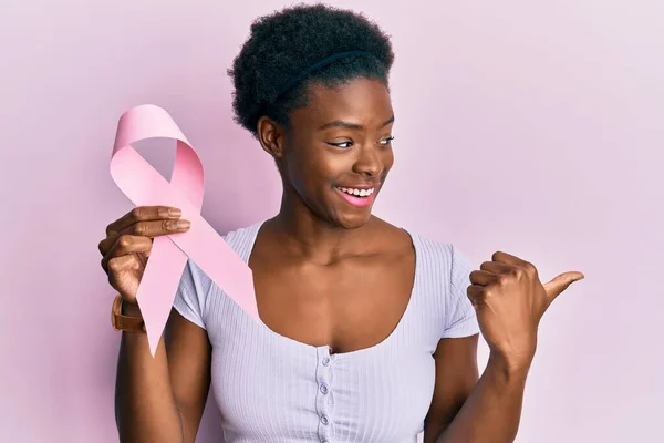 Młoda Afroamerykanka Trzymająca Różową Wstążkę Rakiem Skierowaną Kciukiem Górę Uśmiechnięta — Zdjęcie stockowe