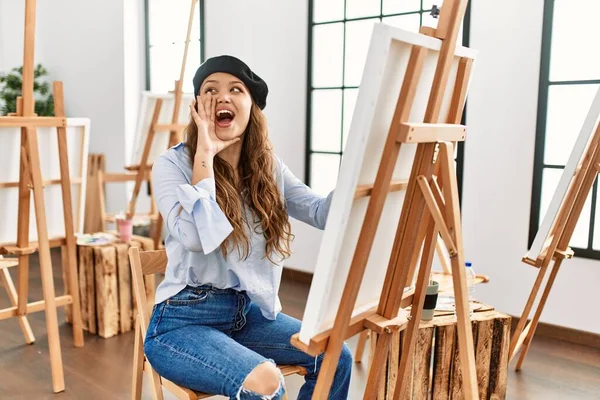 若いヒスパニック系のアーティストの女性は アートスタジオで大声で叫び 口の上に手で横に叫んでキャンバス上で絵を描く コミュニケーションの概念 — ストック写真