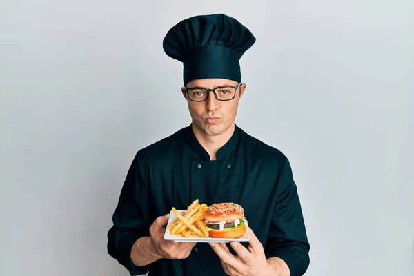 Guapo Joven Chef Sosteniendo Hamburguesa Con Papas Fritas Deprimido Preocuparse —  Fotos de Stock