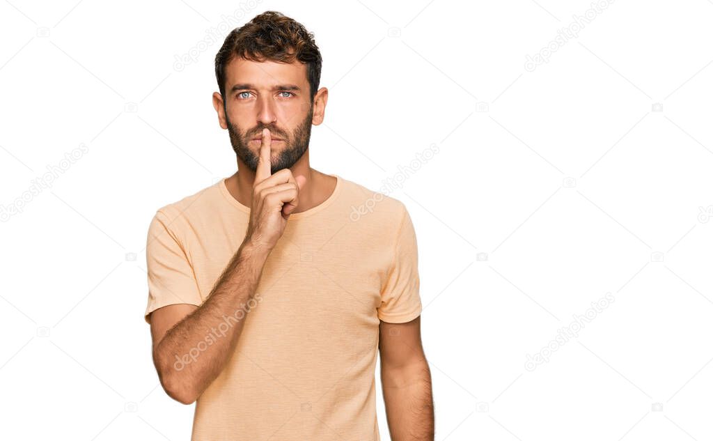 Handsome young man with beard wearing casual tshirt asking to be quiet with finger on lips. silence and secret concept. 