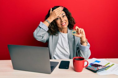 Cpu bilgisayar işlemcisini tutan orta yaşlı güzel bir kadın elleri kafasında, şaşırmış ve sinirli bir yüz ifadesiyle stresli ve sinirli. 