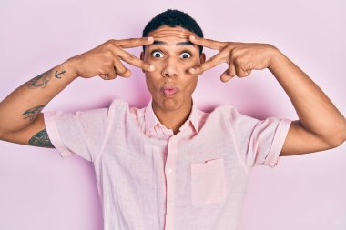 Genç Afro-Amerikalı adam zafer işareti ve barış jesti yapıyor. Ağzı ve şaşı gözleriyle balık suratı yapıyor. Deli ve komik.. 