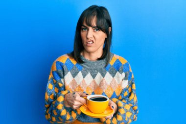 Genç İspanyol kadın bir fincan kahve içiyor habersiz ve kafası karışmış bir ifade. şüphe kavramı. 