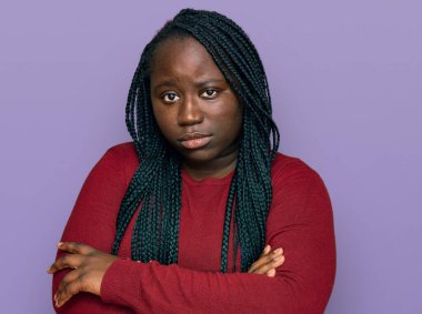 Örgülü, sıradan kıyafetler giyen, kuşkucu ve gergin genç siyahi bir kadın. Yüzünde çapraz kollarla onaylamayan bir ifade var. negatif kişi. 