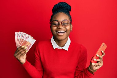 Genç Afrikalı Amerikalı kadın elinde Norveç Kronu banknotları tutarak gülüyor ve kahkahalarla gülüyor.. 