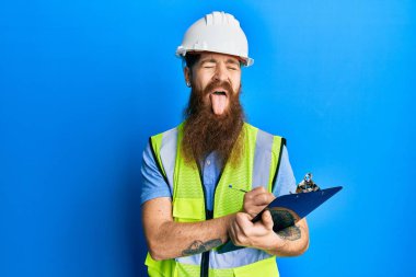 Uzun sakallı, güvenlik kaskı takan, elinde not panosu olan, komik bir ifadeyle dilini dışarı çıkaran kızıl saçlı adam.. 