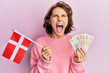Elinde Norveç bayrağı ve Krone banknotları tutan genç esmer kadın kızgın ve kızgın çığlıklar atıyor öfkeyle ve öfkeyle bağırıyor.. 