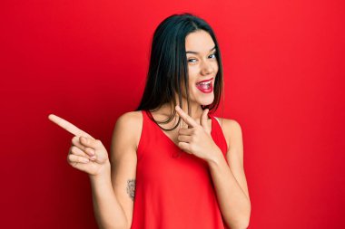 Kolsuz tişörtlü, sıradan giyinen genç İspanyol kız gülümseyip kameraya bakıyor ve iki eliyle ve parmaklarıyla kenarı işaret ediyor.. 