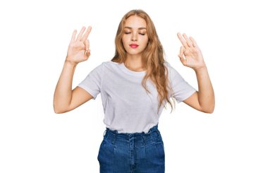 Beyaz günlük tişört giyen genç beyaz kız rahatla ve gözün kapalı gülümse parmaklarınla meditasyon hareketi yap. yoga konsepti. 