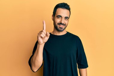 Bir fikir veya soruyla gülümseyen gündelik kıyafetler giyen genç İspanyol adam, bir numara, mutlu bir yüzle işaret ediyor. 