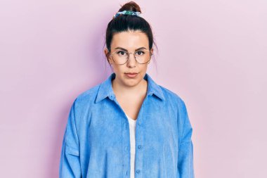 Yüzünde ciddi bir ifade olan günlük kıyafetler ve gözlük takan genç İspanyol kadın. Basit ve doğal bir şekilde kameraya bakıyorsun.. 