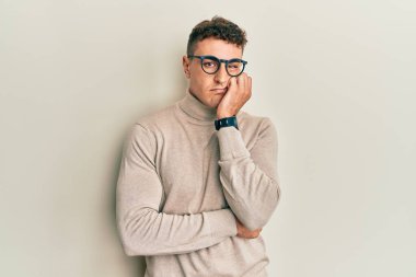 Balıkçı yaka kazak giyen İspanyol genç adam kollarını kavuşturarak depresyondan sıkılmış ve yorgun göründüğünü düşünüyor.. 