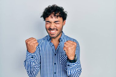 Gündelik kıyafetler giyen genç İspanyol adam başarı için heyecanlı kolları havada ve gözleri kapalı zaferi kutlarken gülümsüyor. Kazanan konsept. 