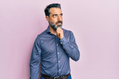 Orta yaşlı, sakallı, gri saçlı, iş kıyafetleri giyen, çenesi üstünde soru soran, düşünceli bir adam. Düşünceli bir yüzle gülümsüyor. şüphe kavramı. 