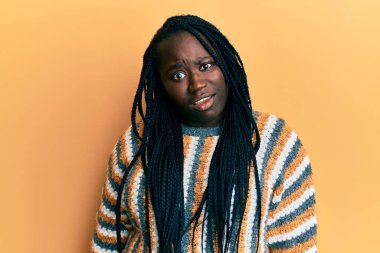 Saçları örgülü genç siyah bir kadın. Şok suratlı, sıradan bir kazak giyiyor. Şüpheci ve alaycı görünüyor. 