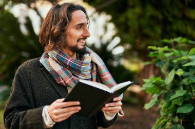 Genç İspanyol adam gülümsüyor. Parkta mutlu bir kitap okuyor..
