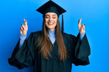 Mezuniyet şapkası ve tören cübbesi giyen güzel esmer kadın umut ve gözlerin kapalı gülümseyerek el sallıyor. Şans ve batıl inançlar. 