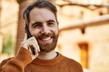 Beyaz sakallı bir adam güneşli bir günde telefonda konuşuyor.