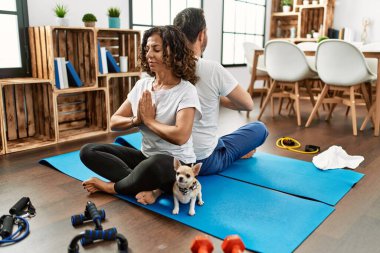 Orta yaşlı İspanyol çift gülümseyerek evde yoga yapıyor..