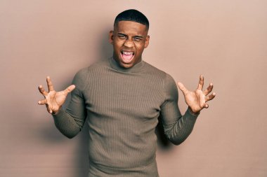 Balıkçı yaka kazak giyen genç siyahi adam deli gibi bağırıyor ve agresif bir ifadeyle bağırıyor ve kollarını kaldırıyor. hüsran kavramı. 