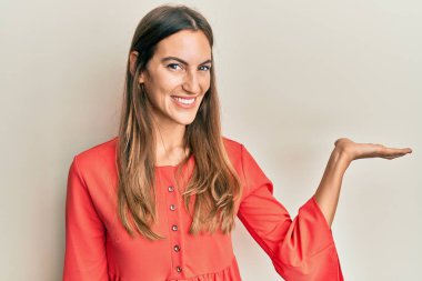 Genç ve güzel bir kadın günlük kıyafetler giyip neşeli bir şekilde gülümsüyor. Elleri avucunun içinde kameraya bakıyor.. 