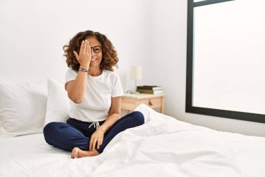 Orta yaşlı İspanyol kadın evinde yatağında oturuyor. Bir gözünü eliyle kapatıyor. Yüzünde kendine güvenen bir gülümseme ve sürpriz bir duygu var.. 