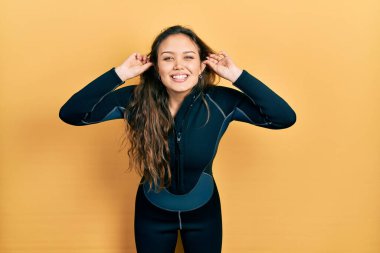 Genç İspanyol kız neoprene üniforması giyiyor gülümsüyor kulakları parmaklarıyla çekiyor, komik bir jest. deneme sorunu 