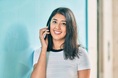 Genç İspanyol kadın gülümsüyor. Şehirdeki akıllı telefondan konuşuyor..