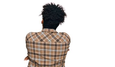 Sakallı, sıradan giyinmiş ve gözlüklü genç Afro-Amerikan adam kollarını kavuşturup arkaya bakıyor. 