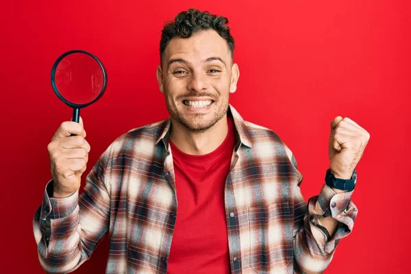 Joven Hispano Sosteniendo Lupa Buscando Mancha Ropa Gritando Orgulloso Celebrando — Foto de Stock