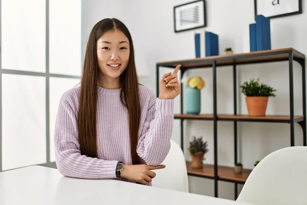 若いです中国の女の子身に着けていますカジュアル服上のテーブルの上に家の笑顔幸せなポインティングとともに手と指で側面 — ストック写真