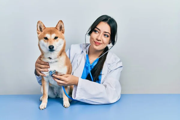 美丽的他的惊慌失措的兽医女人检查狗的健康状况时 面带微笑地看着它的侧面 目不转睛地看着它 — 图库照片