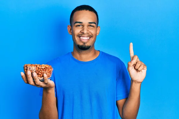 Joven Hombre Afroamericano Sosteniendo Tazón Cacahuetes Sonriendo Con Una Idea — Foto de Stock