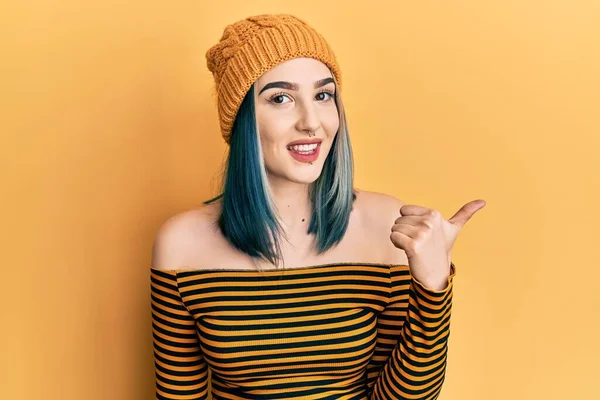 Yün şapka takan, gülümseyen, mutlu yüzlü genç bir kız başparmağıyla yana bakıyor ve işaret ediyor.. 