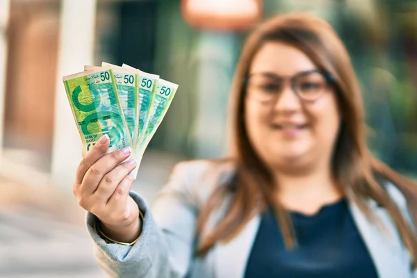 Młoda Hiszpanka Bizneswoman Wielkości Uśmiechnięta Szczęśliwa Trzymając Ręku Banknoty Israel — Zdjęcie stockowe