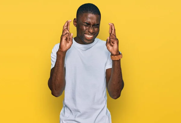 カジュアルな白いTシャツを着た若いアフリカ系アメリカ人男性が希望と目を閉じて笑顔を交わした 幸運と迷信の概念は — ストック写真